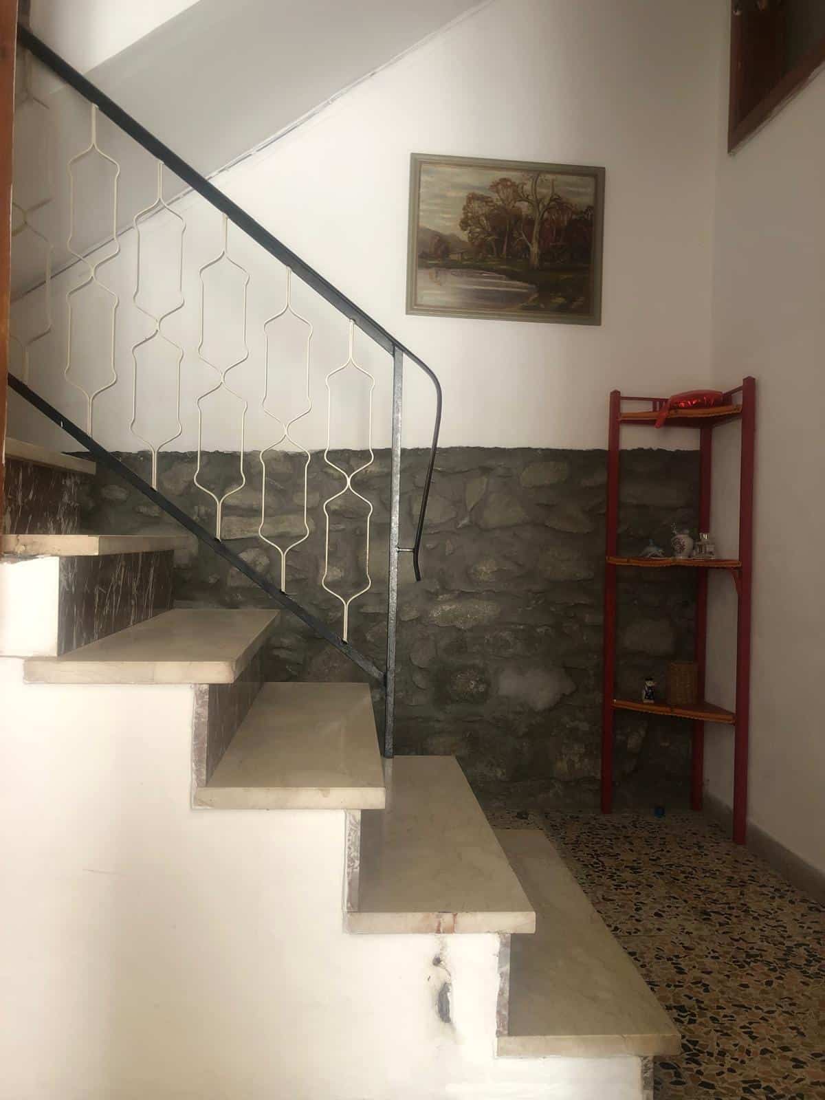 Scalinata interna in pietra con ringhiera decorativa in metallo colorato, parete con pietra a vista, quadri e arredamento rustico, ambiente accogliente e originale, stile casa di montagna, NextCasa.