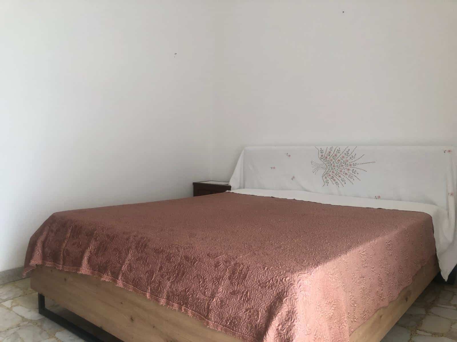 Cottura moderna, camera da letto con letto matrimoniale e copriletto rosa antico, arredamento semplice e spazioso, ideale per soggiorni confortevoli, decorazioni minimaliste, ambiente luminoso e accogliente, stile funzionale per affitti turistici.
