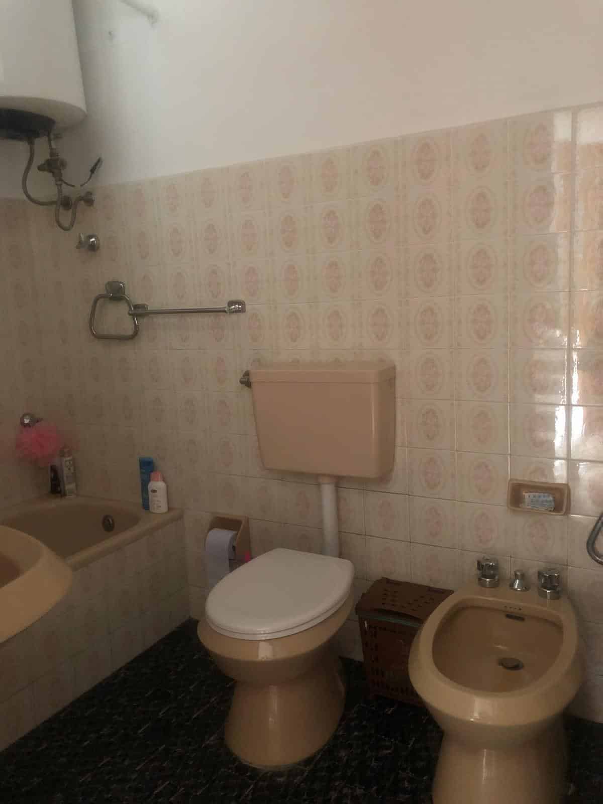 WC bagno con lavabo e bidet in stile vintage, rivestimento in ceramica beige, soluzione di arredamento funzionale e pratico. Ideale per case e appartamenti, con elementi di utilità quotidiana.
