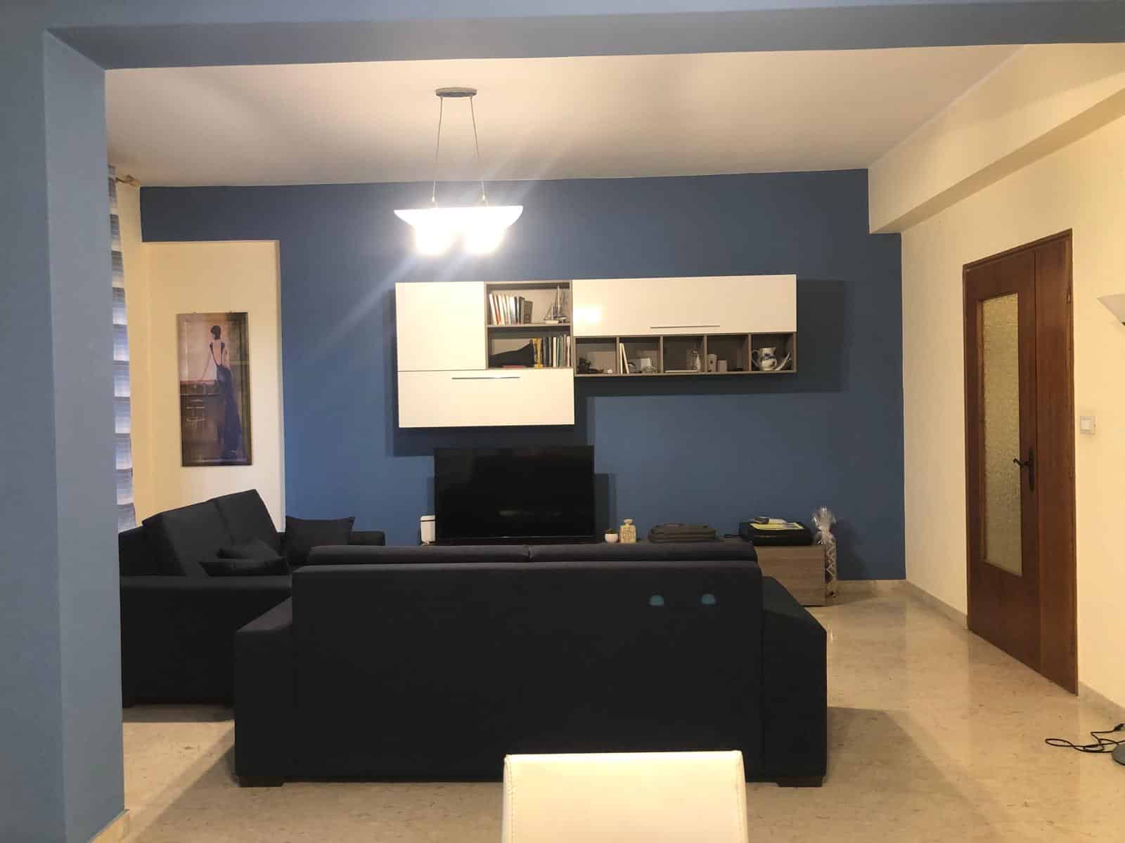 Arredo soggiorno moderno con parete blu, divano nero e mobile TV sospeso. Interior design elegante, ideale per case e appartamenti di design, con mobili su misura e ambienti funzionali.