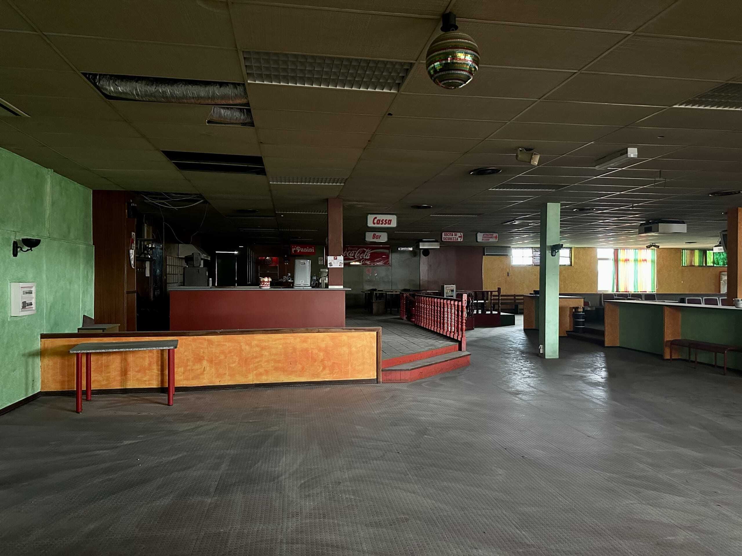 Ampio locale commerciale o discoteca dismessa con pareti colorate e zona bar, illuminazione naturale parziale, pavimento in vinile e ambiente ideale per ristrutturazione o investimento immobiliare.