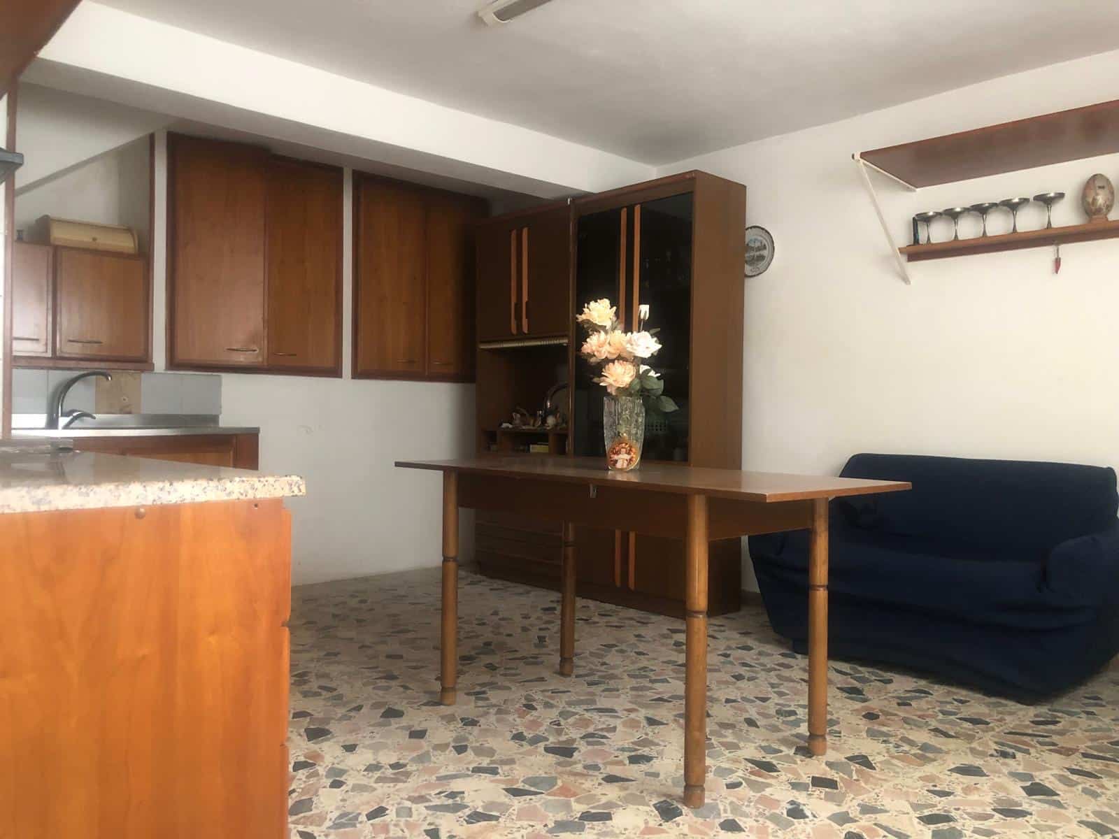 Soggiorno con mobili in legno, divano blu e tavolo in legno elegante, arredamento classico, decorazioni floreali, pavimento in terrazzo, ambiente accogliente e spazioso, ideale per abitazioni accoglienti.