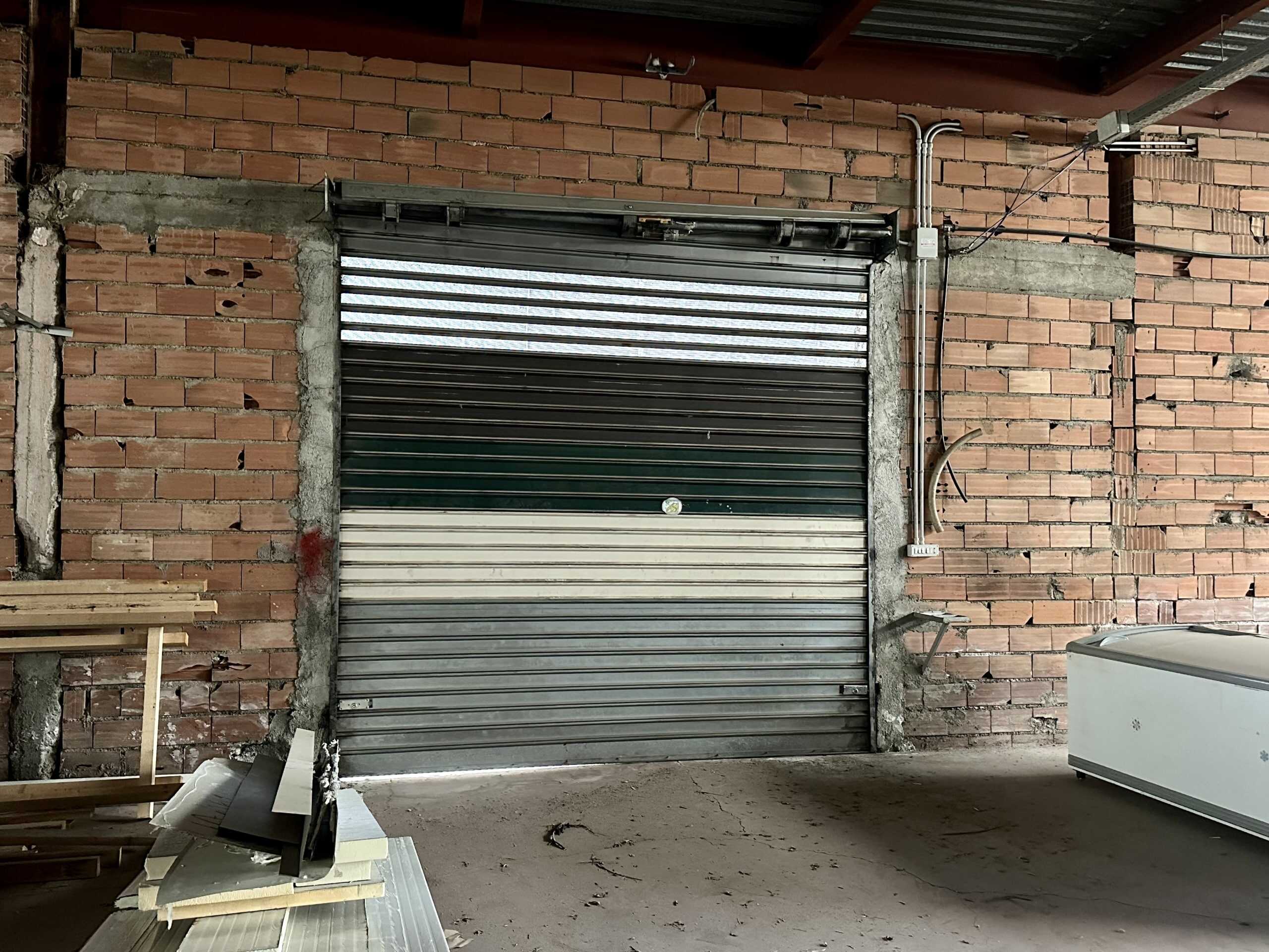Motore industriale con serranda in metallo in fase di installazione in locale commerciale o magazzino. Struttura in laterizi e cemento, con impianti elettrici visibili.