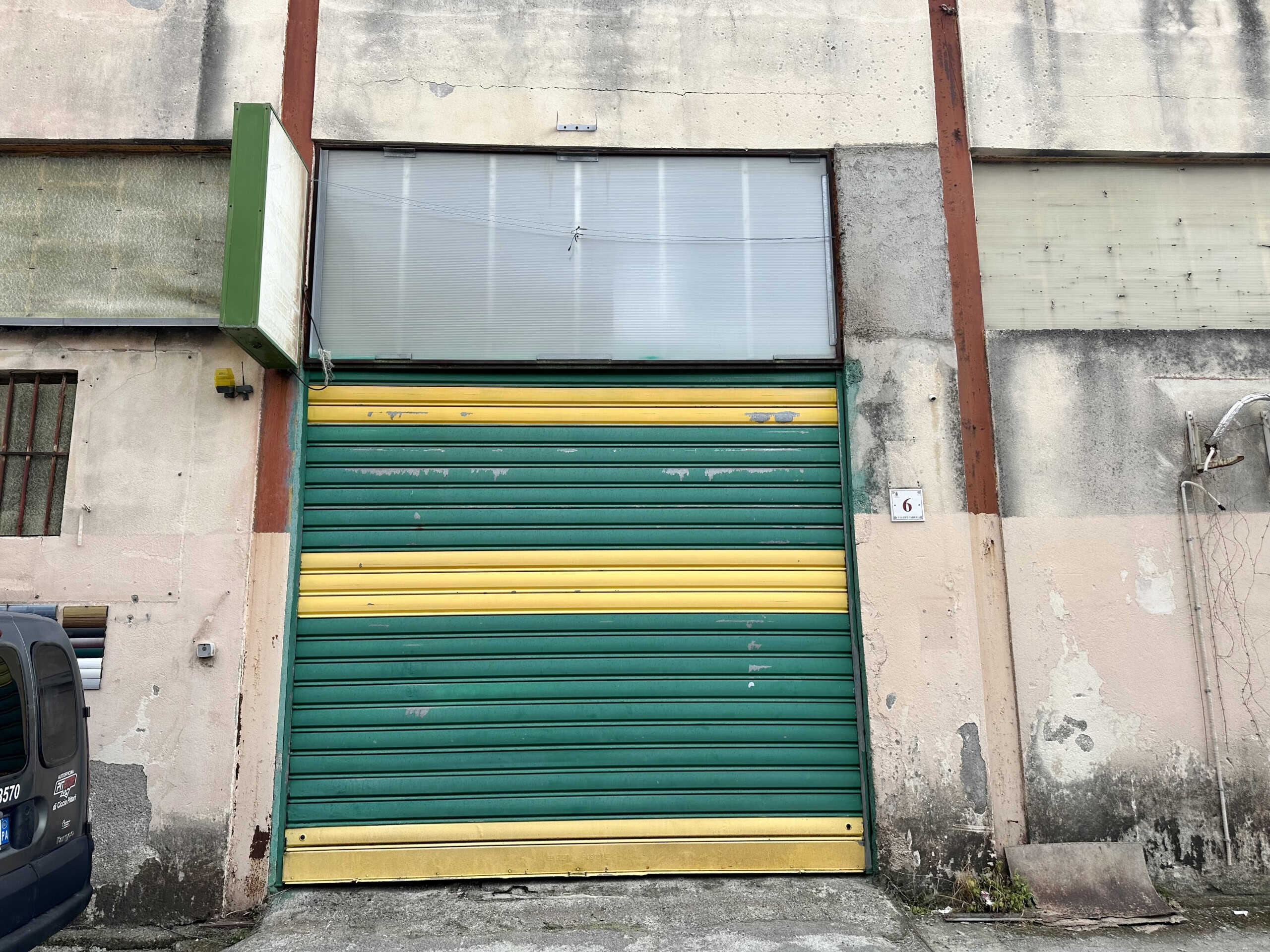 Portone industriale bicolore verde e giallo, ingresso di un magazzino o un deposito, immagine di edificio commerciale in centro città, NextCasa, soluzione di immobili commerciali.