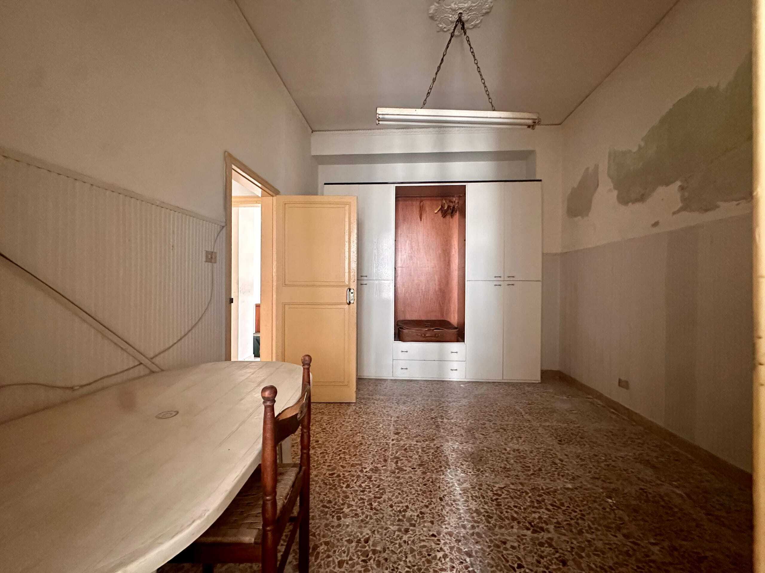 Vecchio ufficio o stanza abitativa in affitto, con armadio a muro bianco e pareti con vernice sbiadita, pavimento in granato e soffitto decorato in stucco, ambiente semplice e da ristrutturare.