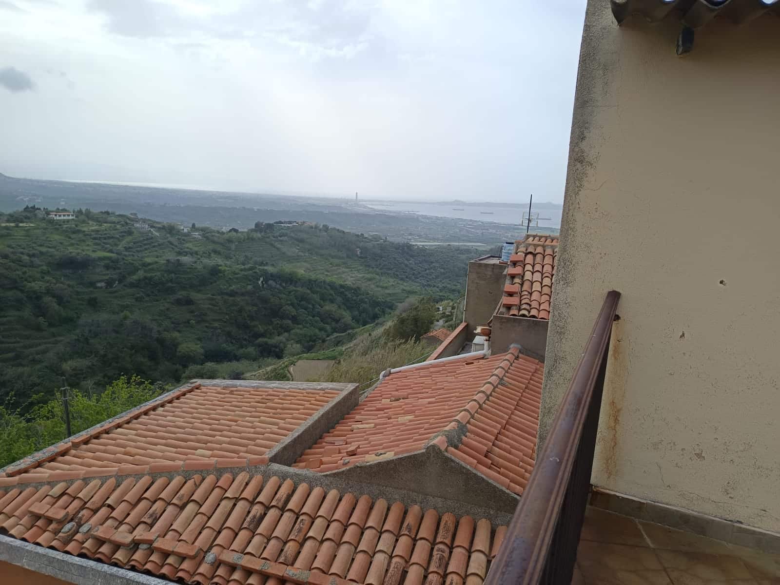 Balcone con vista panoramica su colline e mare, case con tetti in terracotta, paesaggio naturale e immobili, vista di un ambiente residenziale in zona collinare.