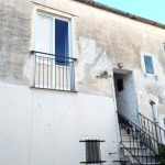 Vecchia casa ristrutturata con balcone e scale esterne, struttura in pietra e facciata in stile rustico. Ideale per investimenti immobiliari e ristrutturazioni a Napoli.
