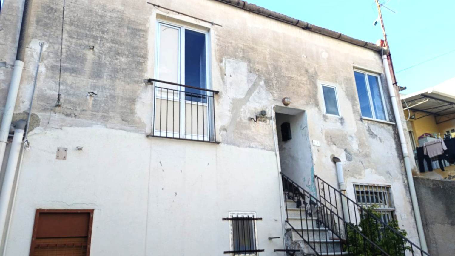 Vecchia casa ristrutturata con balcone e scale esterne, struttura in pietra e facciata in stile rustico. Ideale per investimenti immobiliari e ristrutturazioni a Napoli.