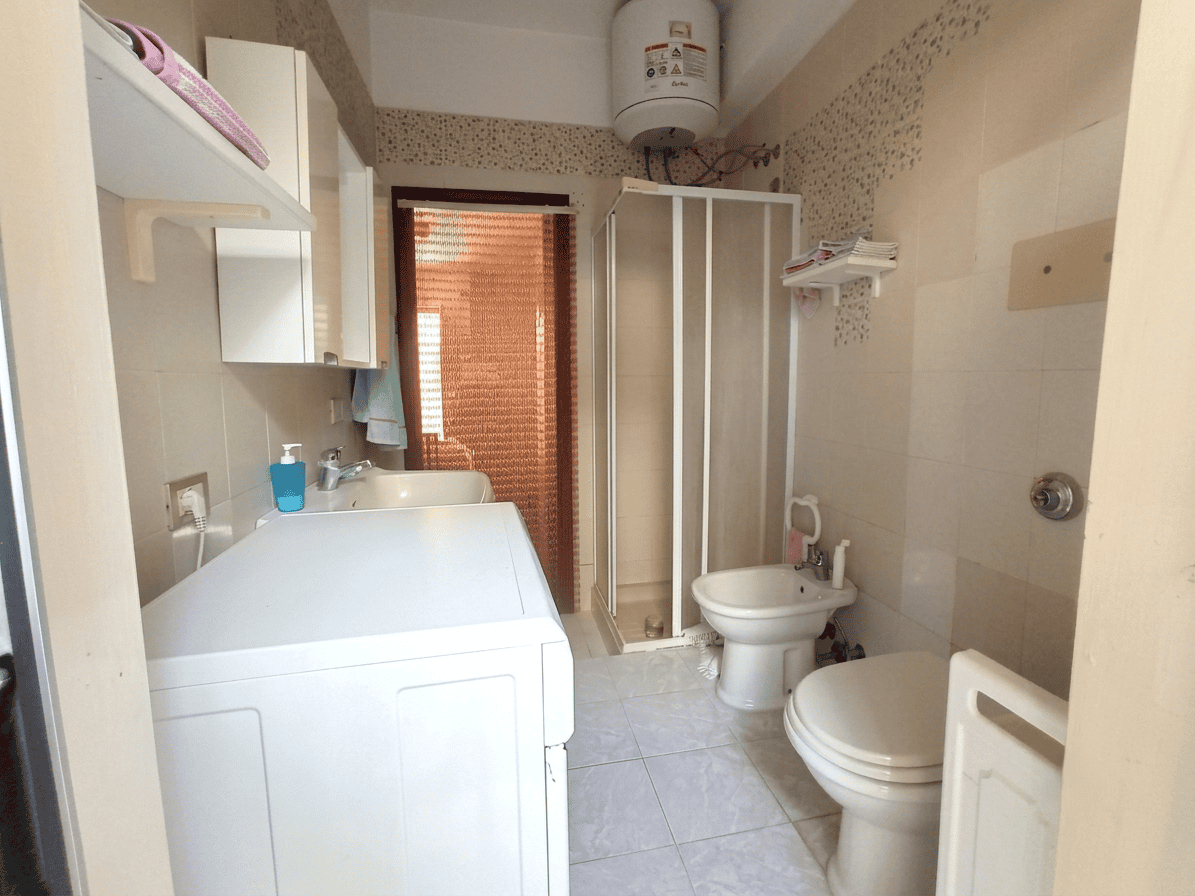 Interno di un bagno in un appartamento in vendita a Oliveri, con lavatrice, doccia, WC e bidet, arredato in modo semplice.