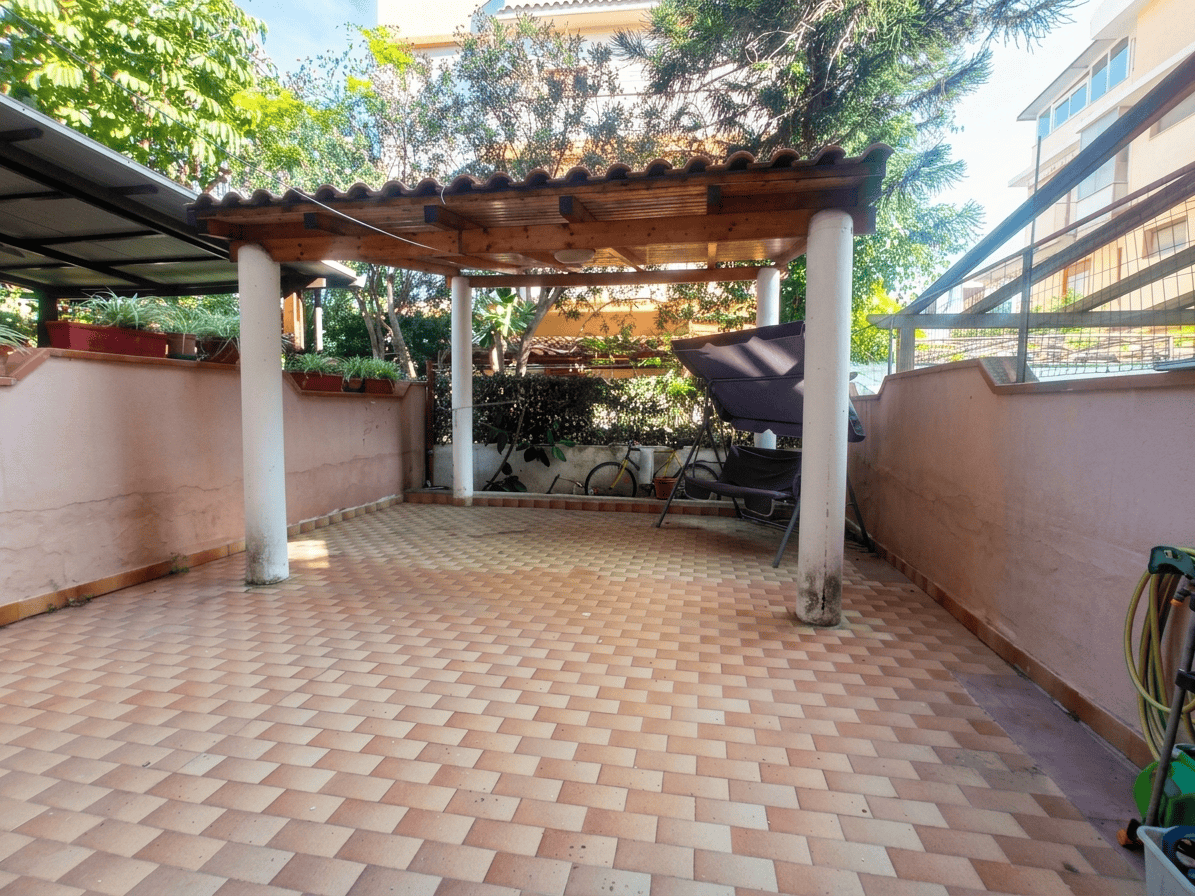 Ampia terrazza privata con copertura in legno, pavimentazione in piastrelle e vista su giardino e edifici circostanti a Oliveri, Me.
