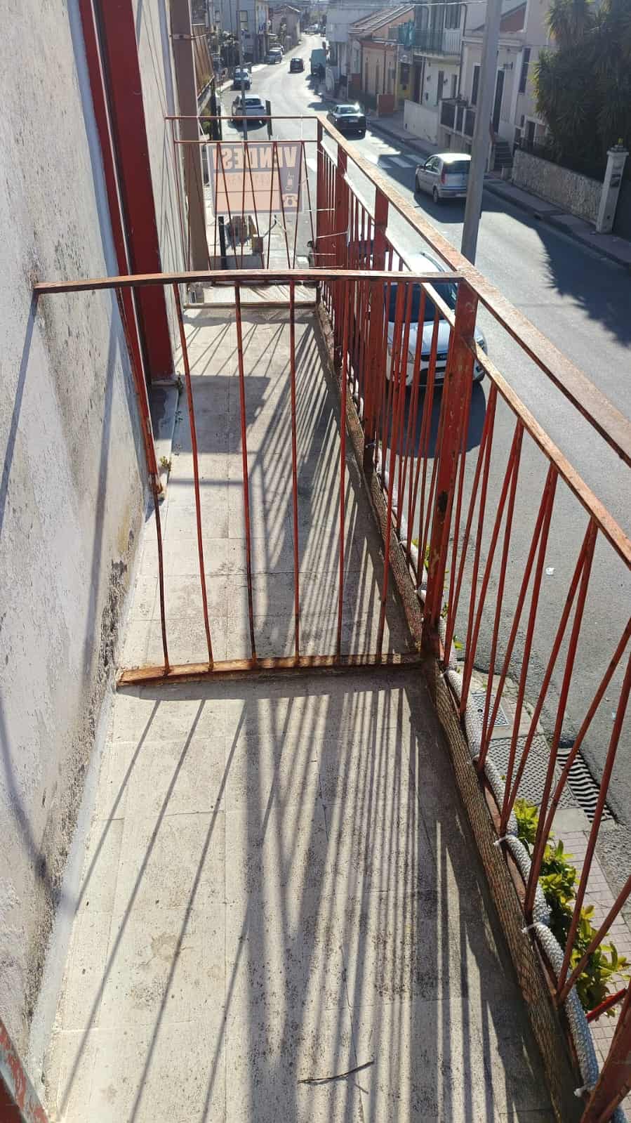 Sistema di balcone in ferro battuto rovinato, balcone di un appartamento in zona residenziale, vista sulla strada con auto e edifici di città. Potrebbe necessitare di restauro o manutenzione.