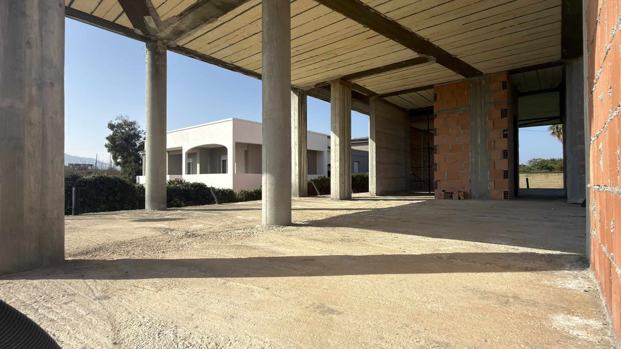 Ampio spazio esterno di una casa in costruzione con colonne in cemento e pareti in mattoni, pronto per essere completato con finiture e dettagli architettonici.