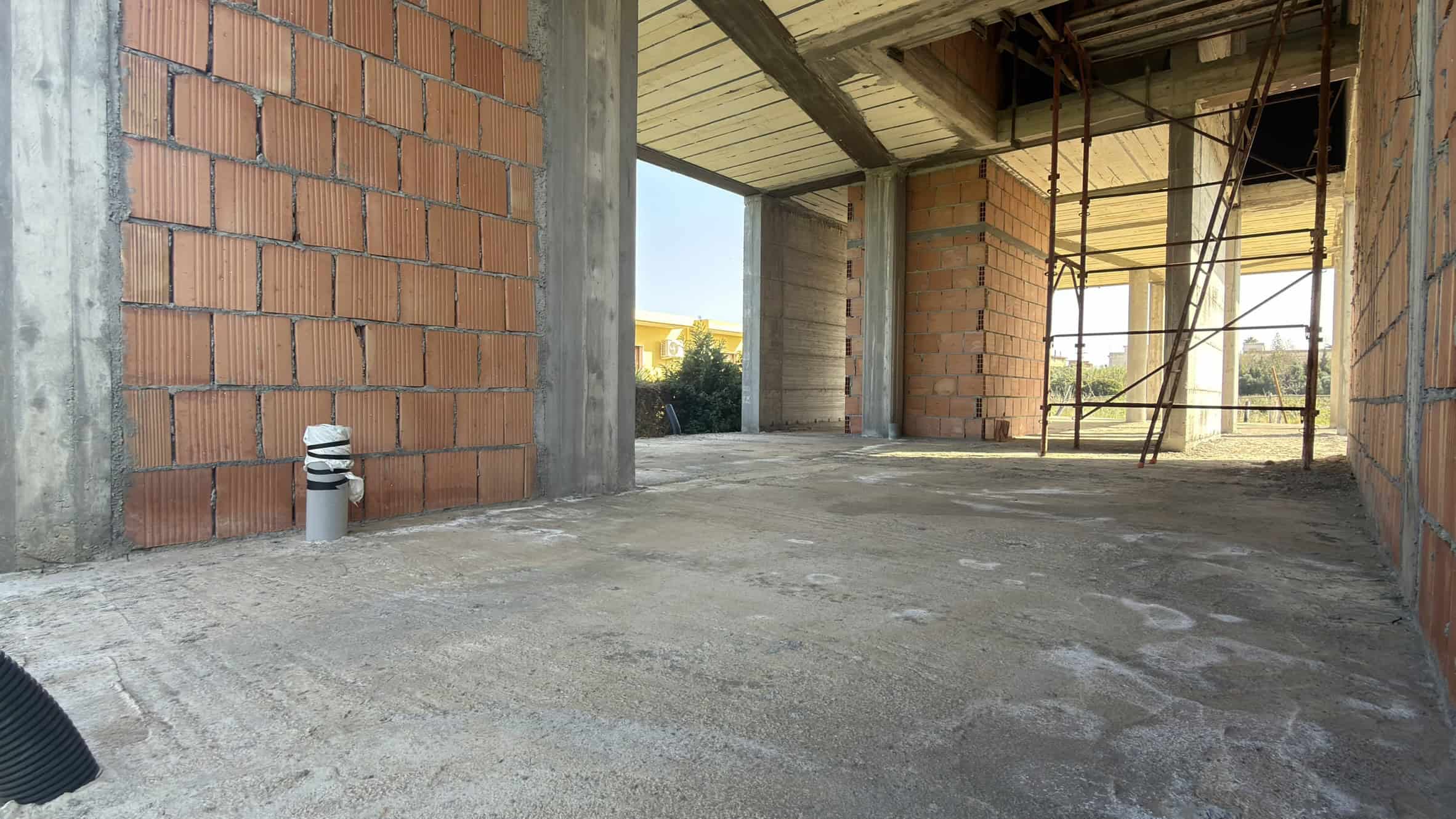 Pannello di costruzione di una casa in fase di realizzazione con pareti in mattoni e struttura in cemento armato, vista dall'interno con scaffalature e apertura verso l'esterno.