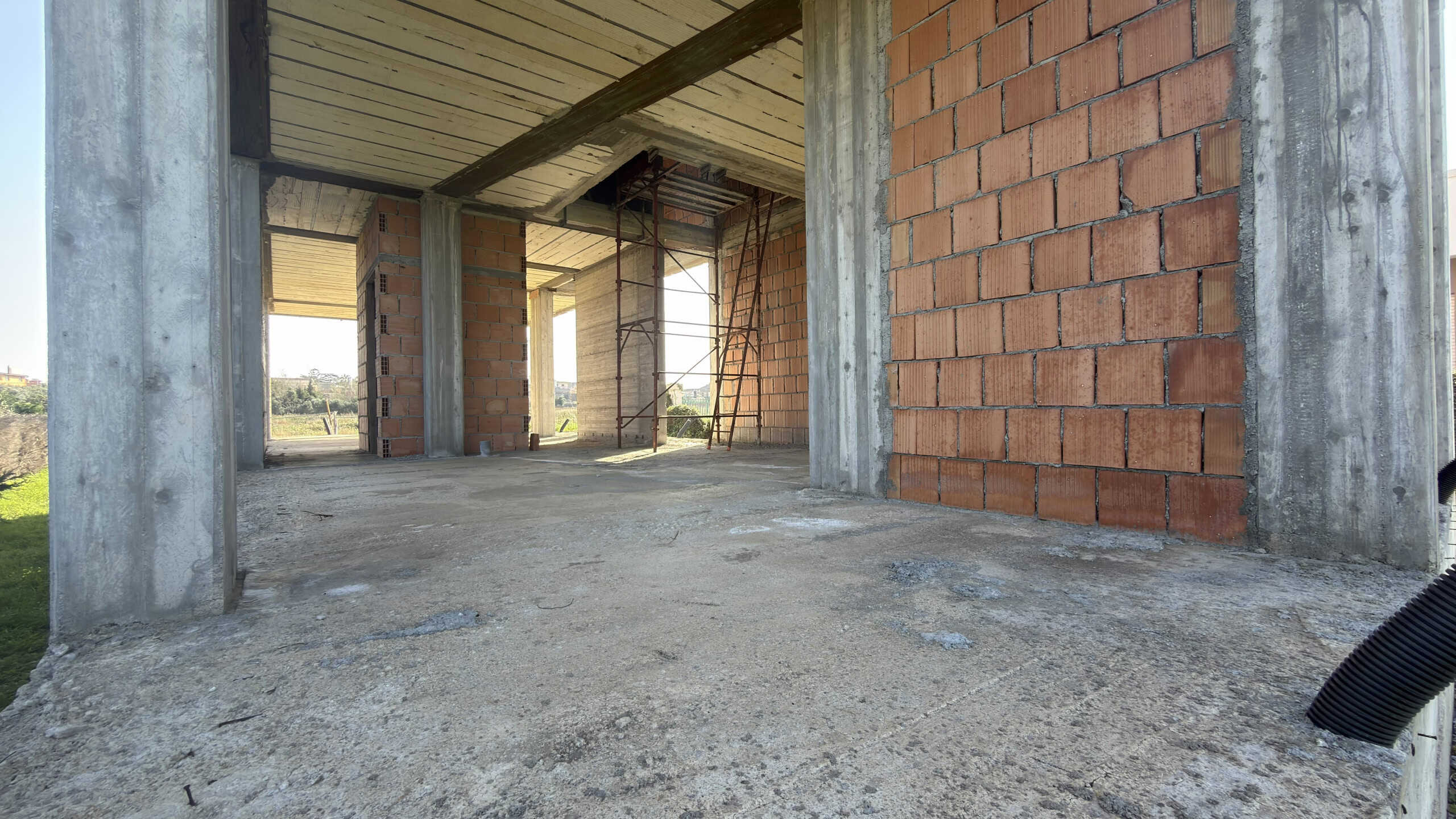 Pannello di costruzione di un edificio residenziale in fase di realizzazione con struttura in cemento e mattoni rossi, scaffalature e ponteggi visibili all’interno.