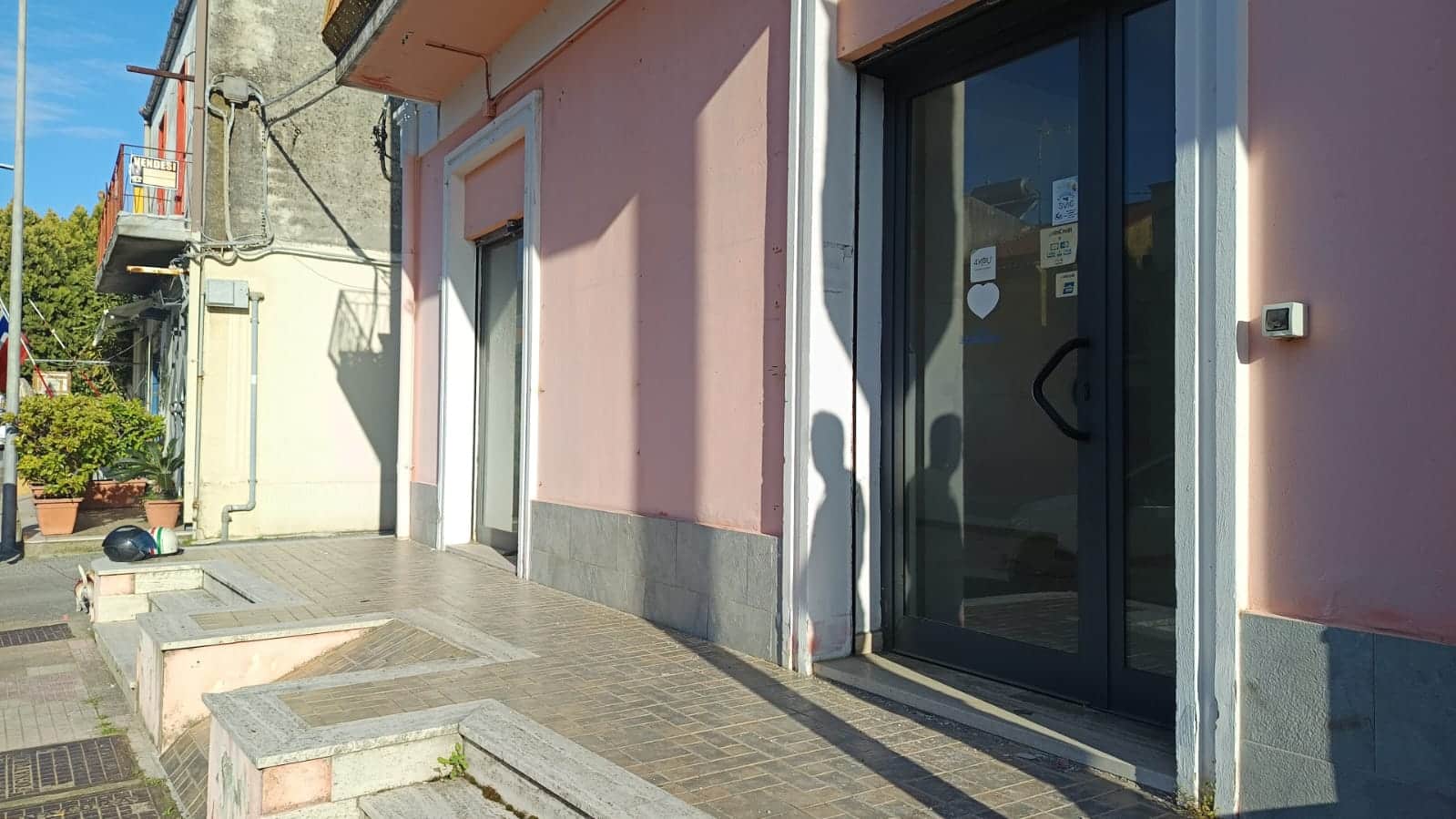 Ampio ingresso con porta scorrevole in vetro e facciata rosa, ideale per negozio o attività commerciale, con arredo urbano e ambiente luminoso, perfetto per valorizzare gli spazi commerciali.