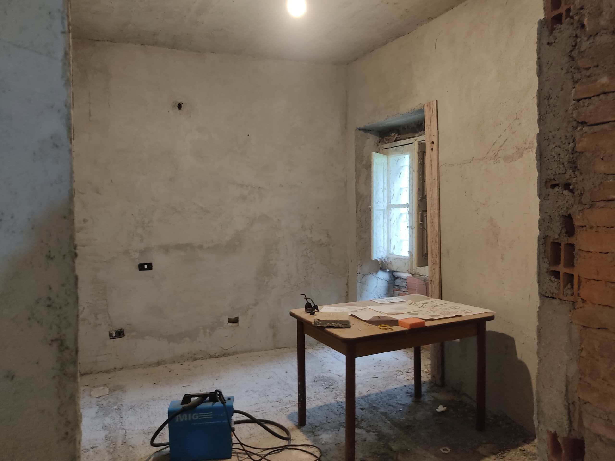 Finestra da ristrutturare in una stanza di casa in fase di rinnovamento, con pareti grezze e spazio di lavoro, rappresenta un progetto di ristrutturazione edilizia con attenzione ai dettagli e alle finiture.