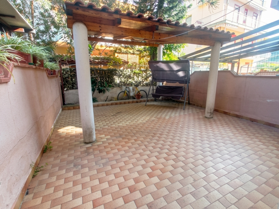 Spazio esterno con pavimentazione in piastrelle, copertura in legno e area relax con sedie a sdraio, ideale per vivere all'aperto in zona residenziale a Oliveri.