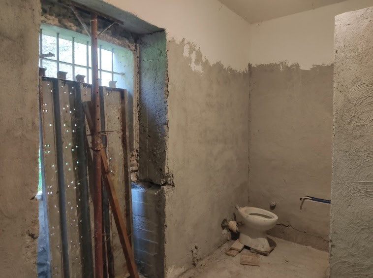 Sconda di un bagno in ristrutturazione con pareti grezze e un wc installato, finestre per l’illuminazione naturale, elementi di costruzione visibili e lavoro in corso per il rifacimento degli interni.