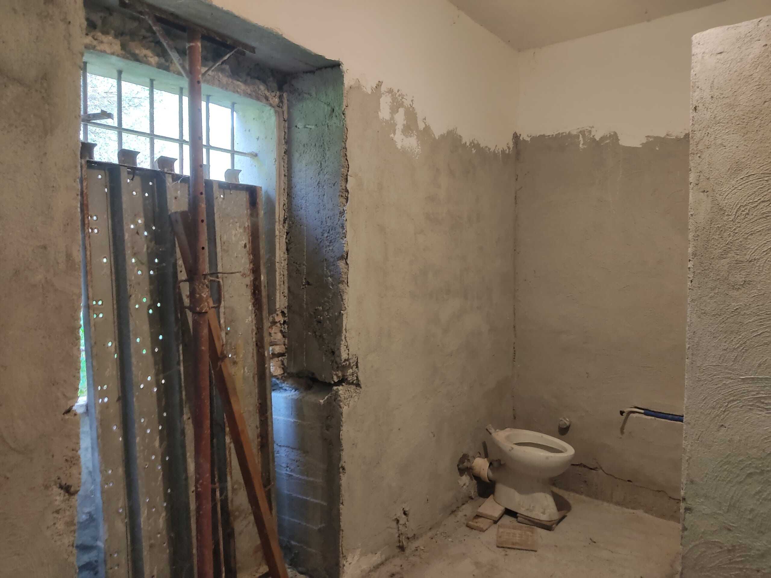 Sconda di un bagno in ristrutturazione con pareti grezze e un wc installato, finestre per l’illuminazione naturale, elementi di costruzione visibili e lavoro in corso per il rifacimento degli interni.