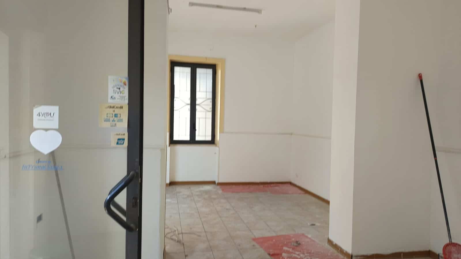 Spazio interno di un appartamento in fase di ristrutturazione, con pareti bianche, finestra con grate e pavimento in lavorazione, pronto per essere arredato e abitato.