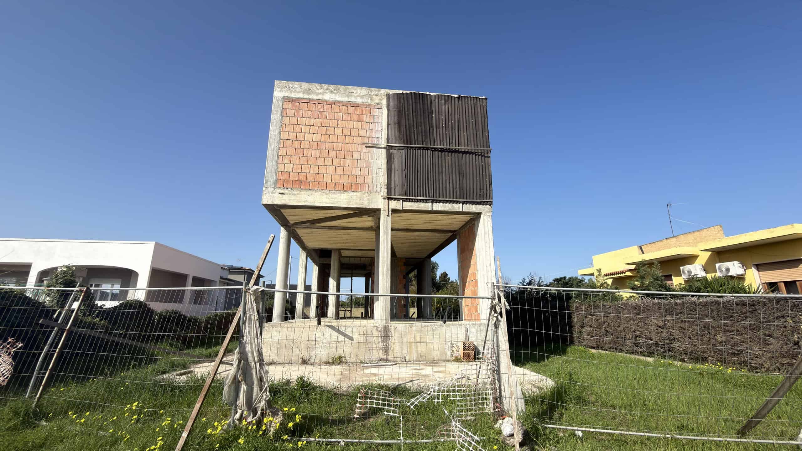 Villa in costruzione con struttura in cemento e mattoni, situata in un'area residenziale verde e tranquilla, pronta per essere completata e personalizzata secondo le esigenze.