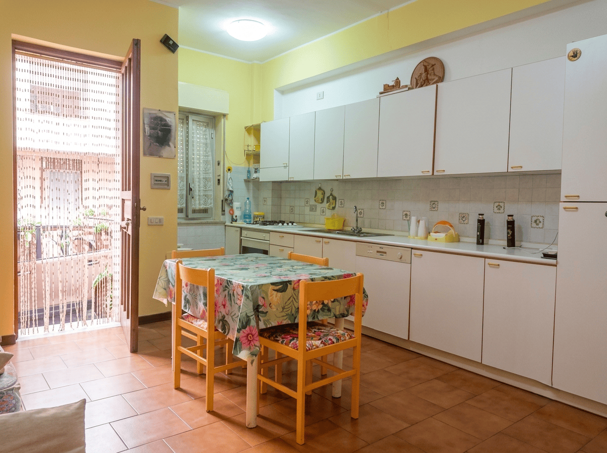 Cucina spaziosa e luminosa con mobili bianchi e tavolo da pranzo colorato in un appartamento in vendita a Oliveri, Me.