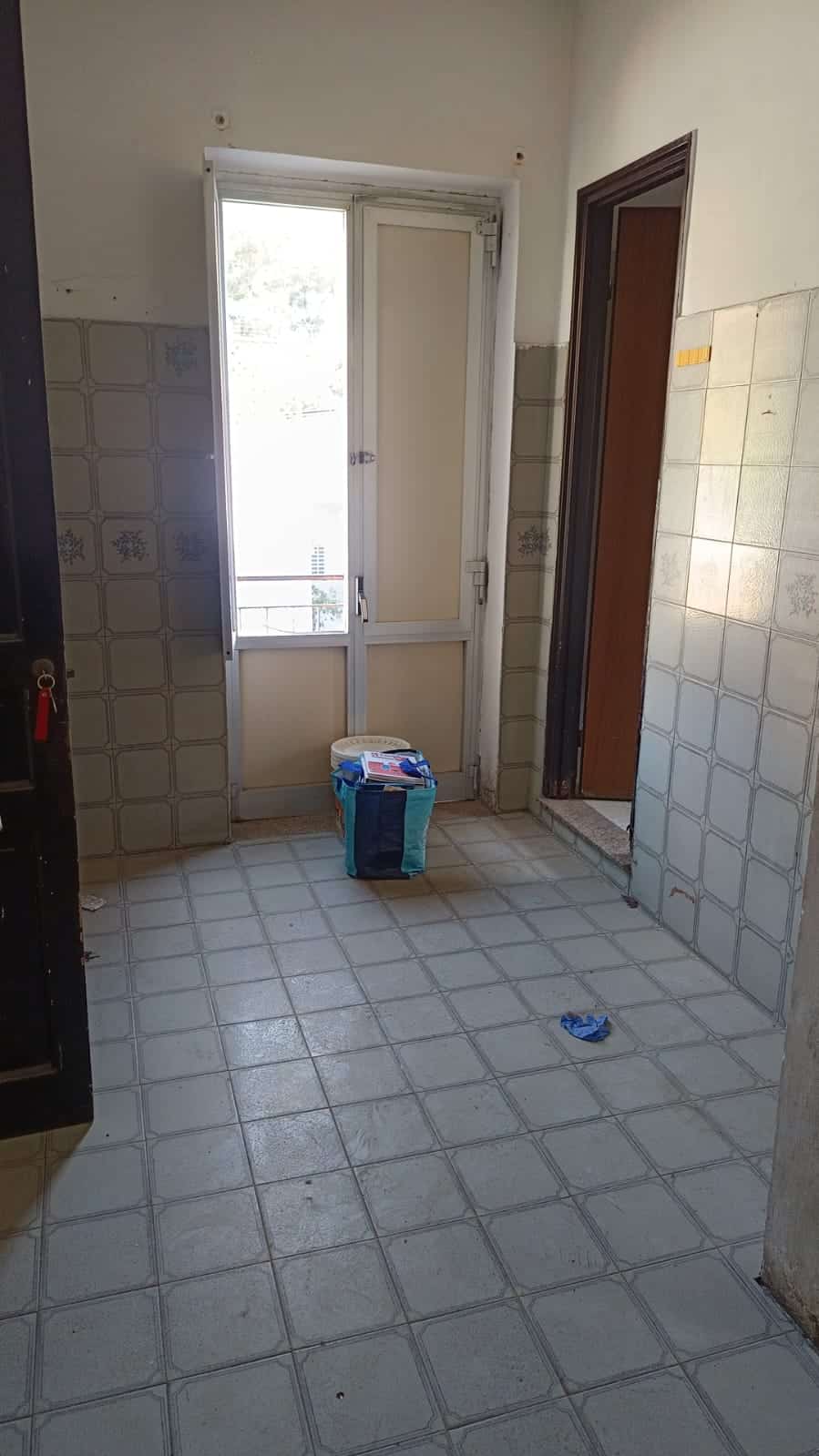 Portafinestra con balcone e rivestimento di piastrelle in cucina, spazi abitativi luminosi, dettagli interni di case in vendita a NextCasa, immobile da ristrutturare.