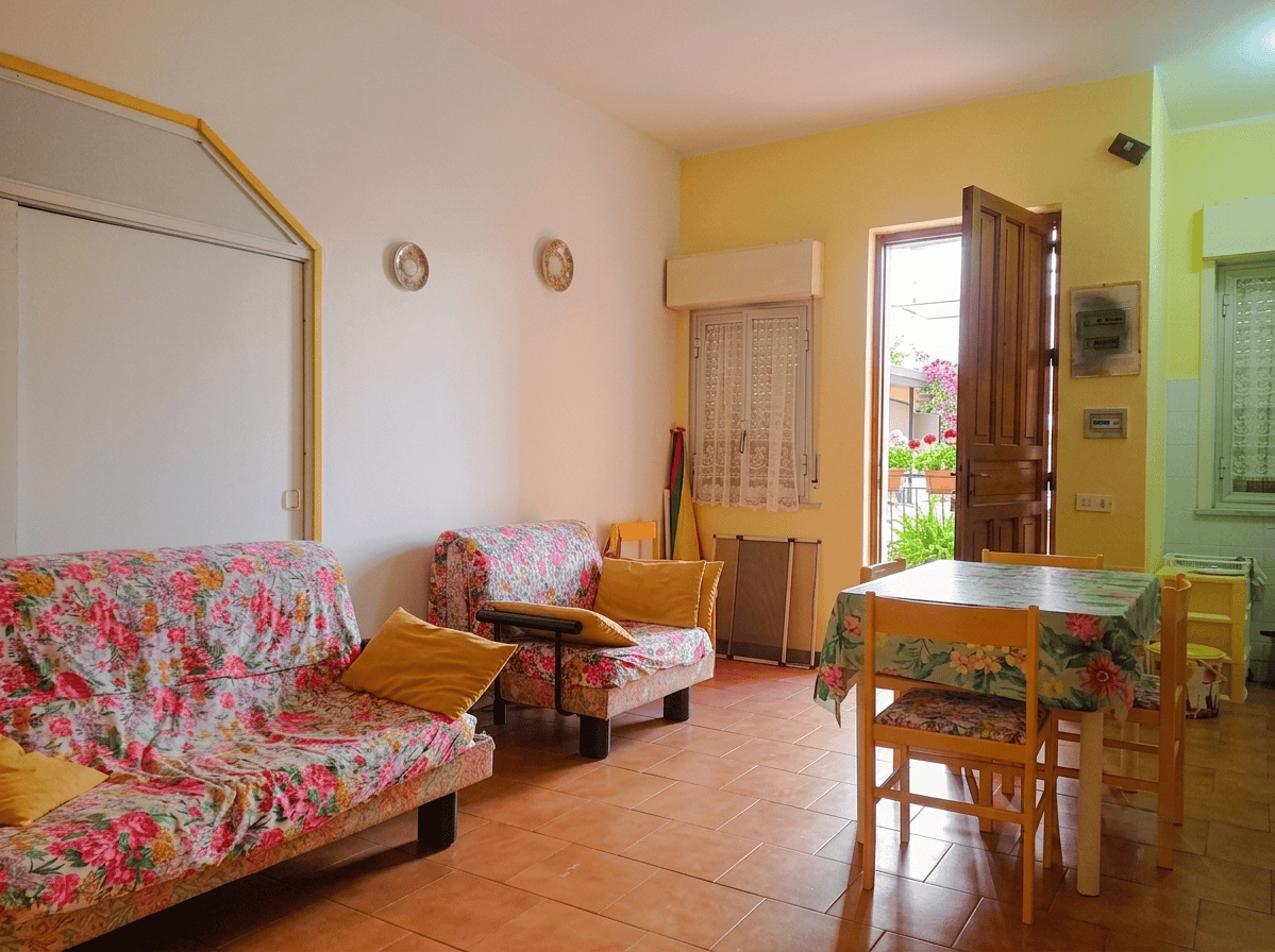 Interno di un appartamento con soggiorno, divani, tavolo e accesso al balcone, luminoso e accogliente.
