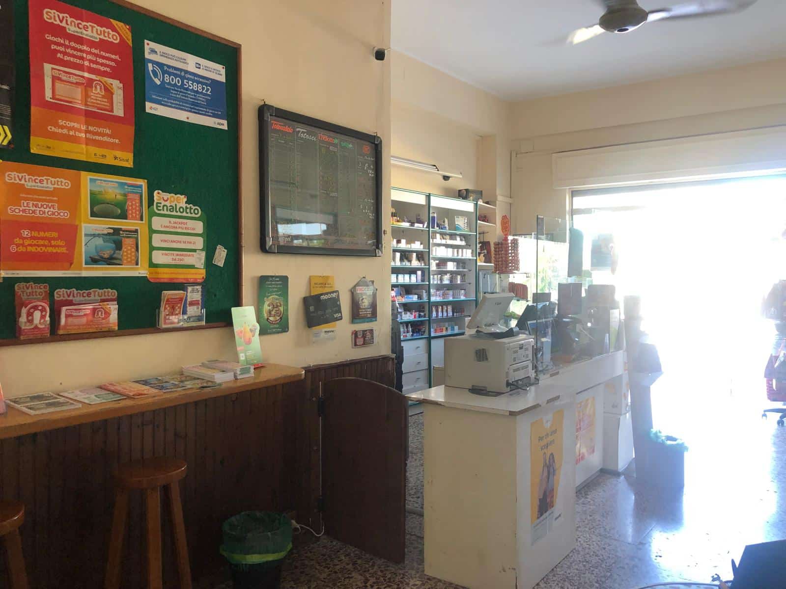 Registratore di cassa e scaffali con prodotti in un negozio di quartiere NextCasa, punto vendita di servizi e vendita di tabacchi, lotto, gratta e vinci, e biglietti di trasporto pubblico, situato in un ambiente luminoso e accogliente.