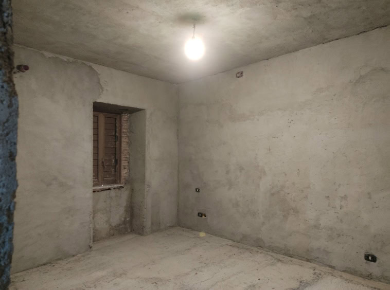 Immagine di una stanza in fase di ristrutturazione, con pareti grezze e senza finiture, pronta per essere rifinita.