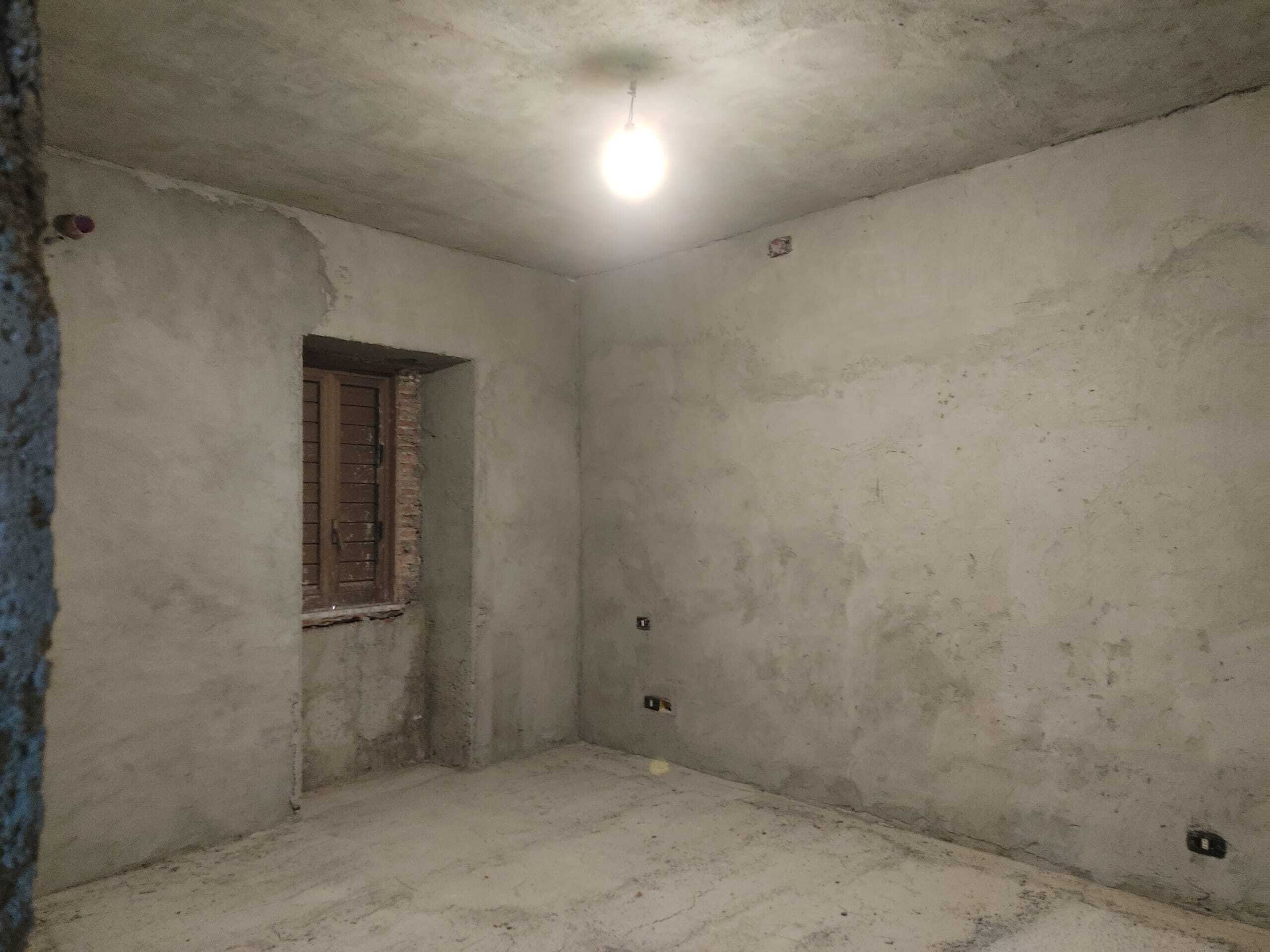 Immagine di una stanza in fase di ristrutturazione, con pareti grezze e senza finiture, pronta per essere rifinita.