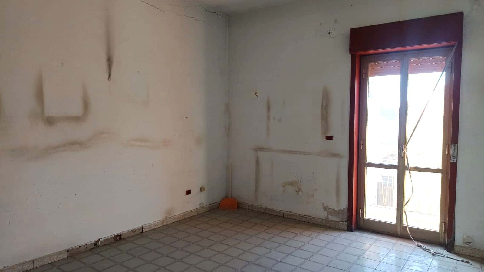 Villetta in ristrutturazione, interno vuoto con pareti da restaurare e porta finestra con vista su balcone, ideale per progetti di ristrutturazione o investimento immobiliare.