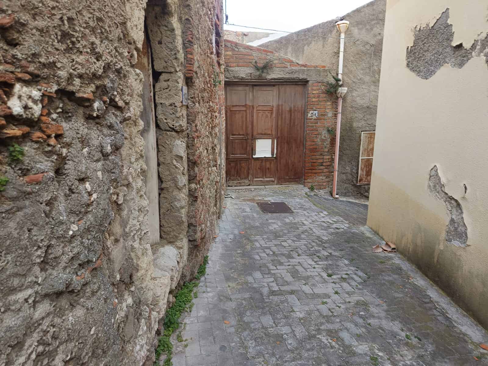 Vecchio vicolo di pietra con porta in legno e pareti in pietra e cemento, angolo di strada in ambientazione storica, tipico quartiere residenziale italiano.