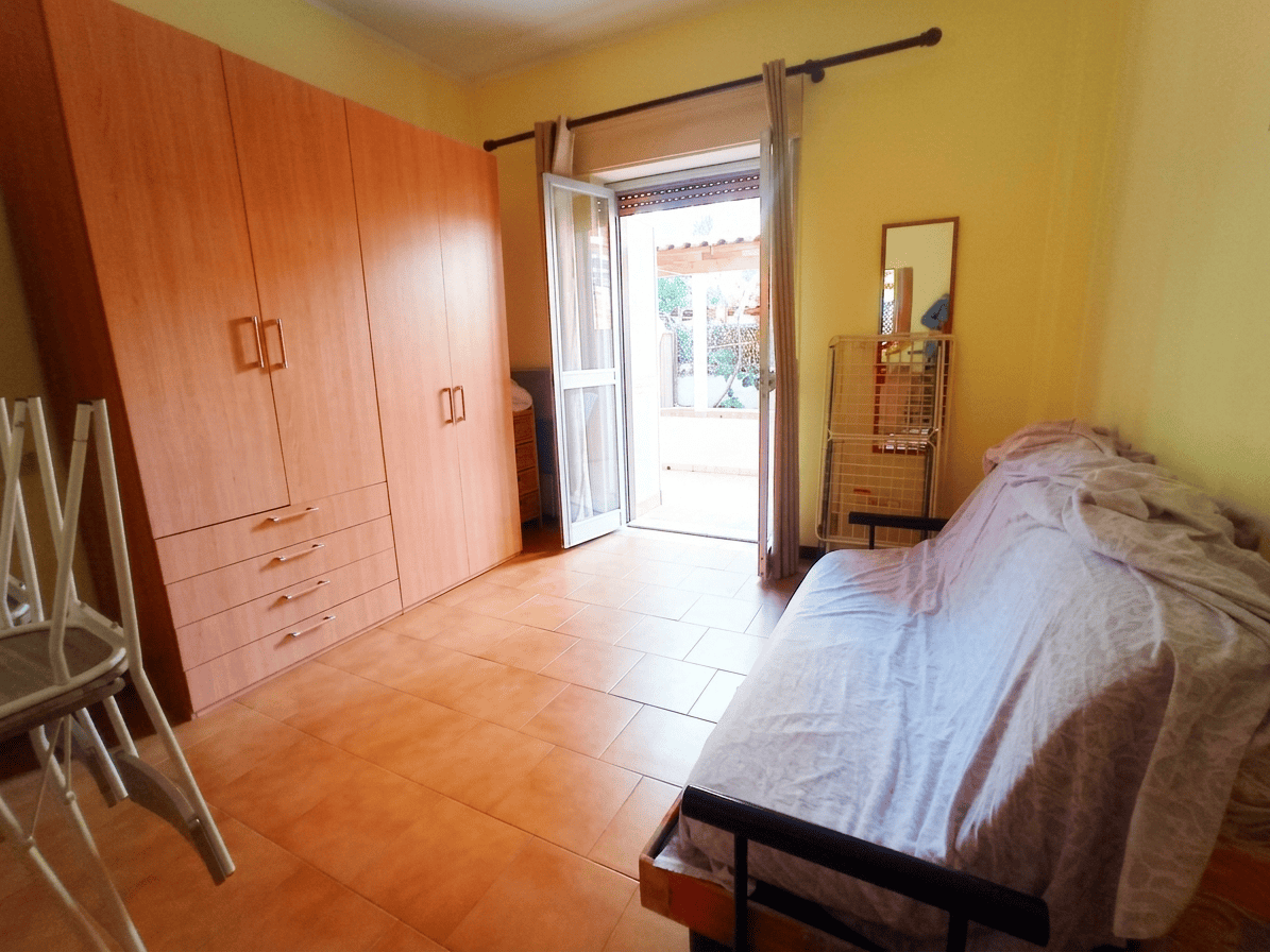 Camera da letto luminosa con accesso al balcone, armadio grande e letto coperto da una coperta chiara, in un appartamento in vendita a Oliveri.