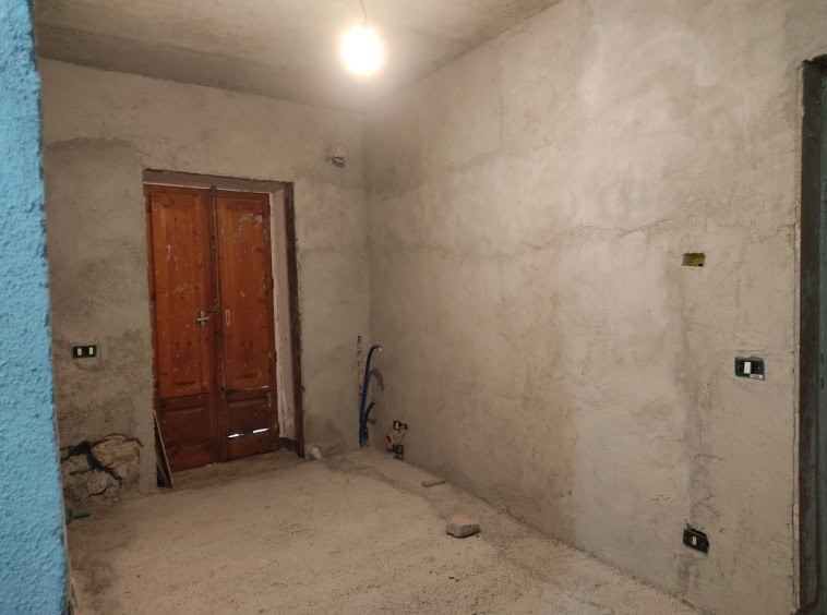 Parete in fase di ristrutturazione, pronto per finiture e impianti elettrici, con porta in legno e muro grezzo, ideale per progetti di interior design.