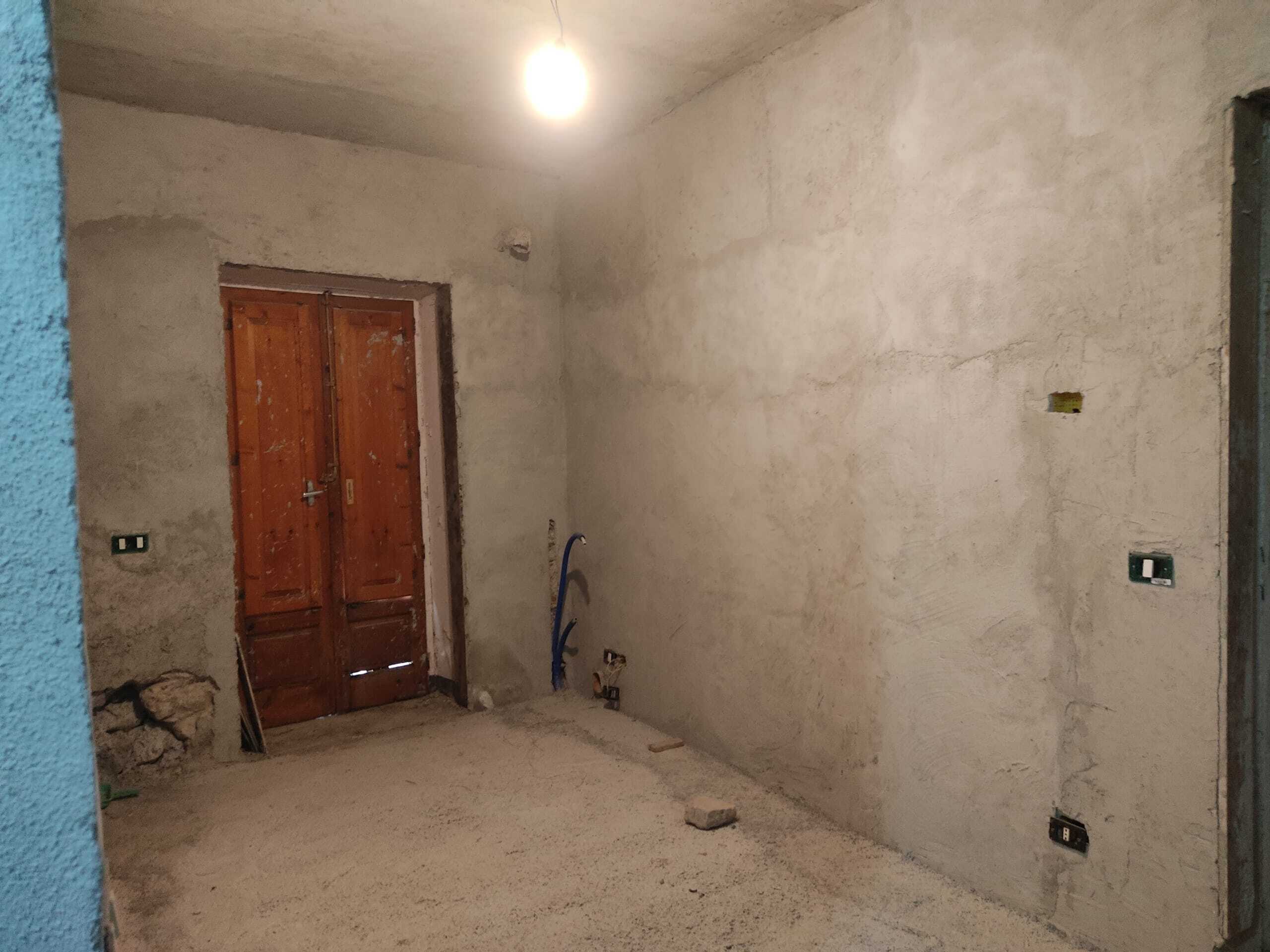 Parete in fase di ristrutturazione, pronto per finiture e impianti elettrici, con porta in legno e muro grezzo, ideale per progetti di interior design.