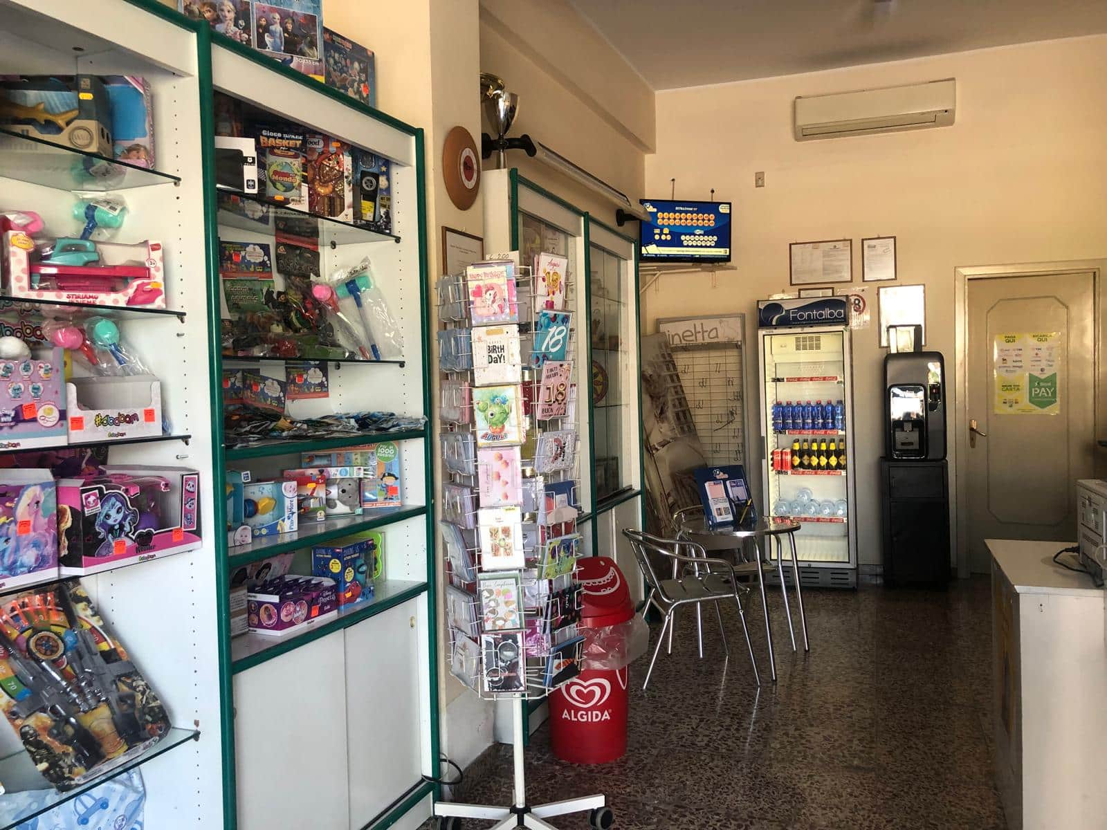 Vendita di giocattoli e articoli di cancelleria in negozio con espositori di prodotti per bambini e adulti, ambiente accogliente e ben organizzato adatto a comprare regali o semplici acquisti quotidiani.