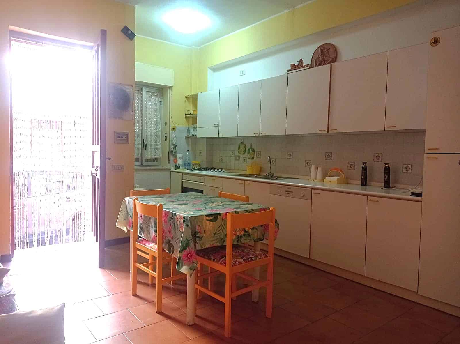 E cucina abitabile con tavolo da pranzo e illuminazione naturale dalla finestra e porta balcone, mobili in stile semplice, ambiente accogliente e funzionale, ideale per famiglie e investimenti immobiliari.