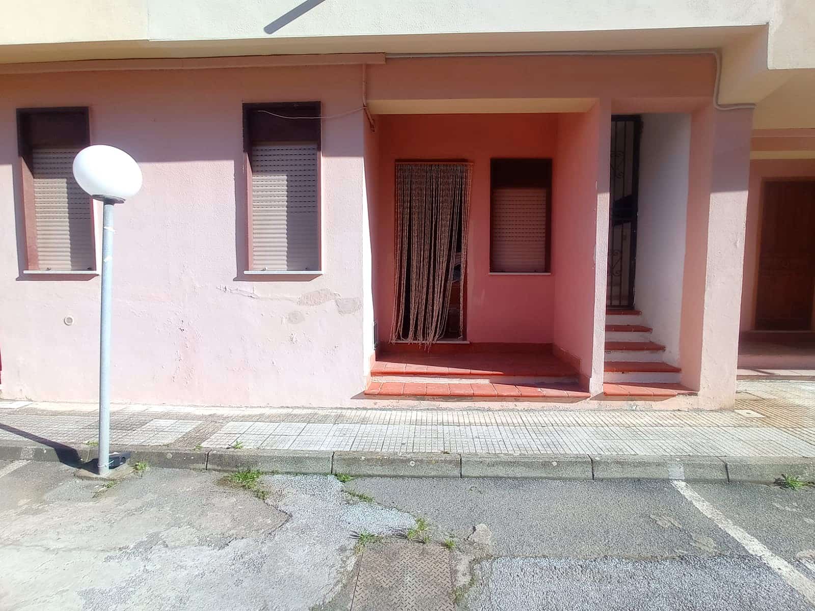 Balcone e ingresso di una casa residenziale con facciata rosa, persiane, scale e barriera di sicurezza, ambiente esterno con marciapiede e lampione in stile moderno, ideale per immobiliare e compravendite.