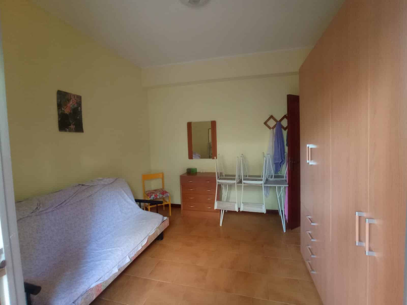 Letto singolo con copriletto a fiori, camera da letto semplice e funzionale, con armadio e mobiletto in legno, ambiente luminoso e accogliente, ideale per locazioni di breve o lungo termine.