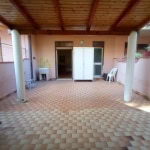 Spazio esterno coperto in appartamento con piastrelle beige, colonne bianche, area relax con sedie, lavabo e accessori in stile mediterraneo, ideale per casa con terrazza o giardino.