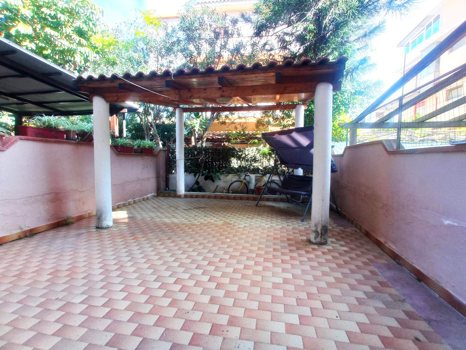 Spazio esterno privato con pergolato in legno, pavimentazione in cotto, piante in vaso e ambiente tranquillo, ideale per relax, barbecue e convivialità all'aperto.
