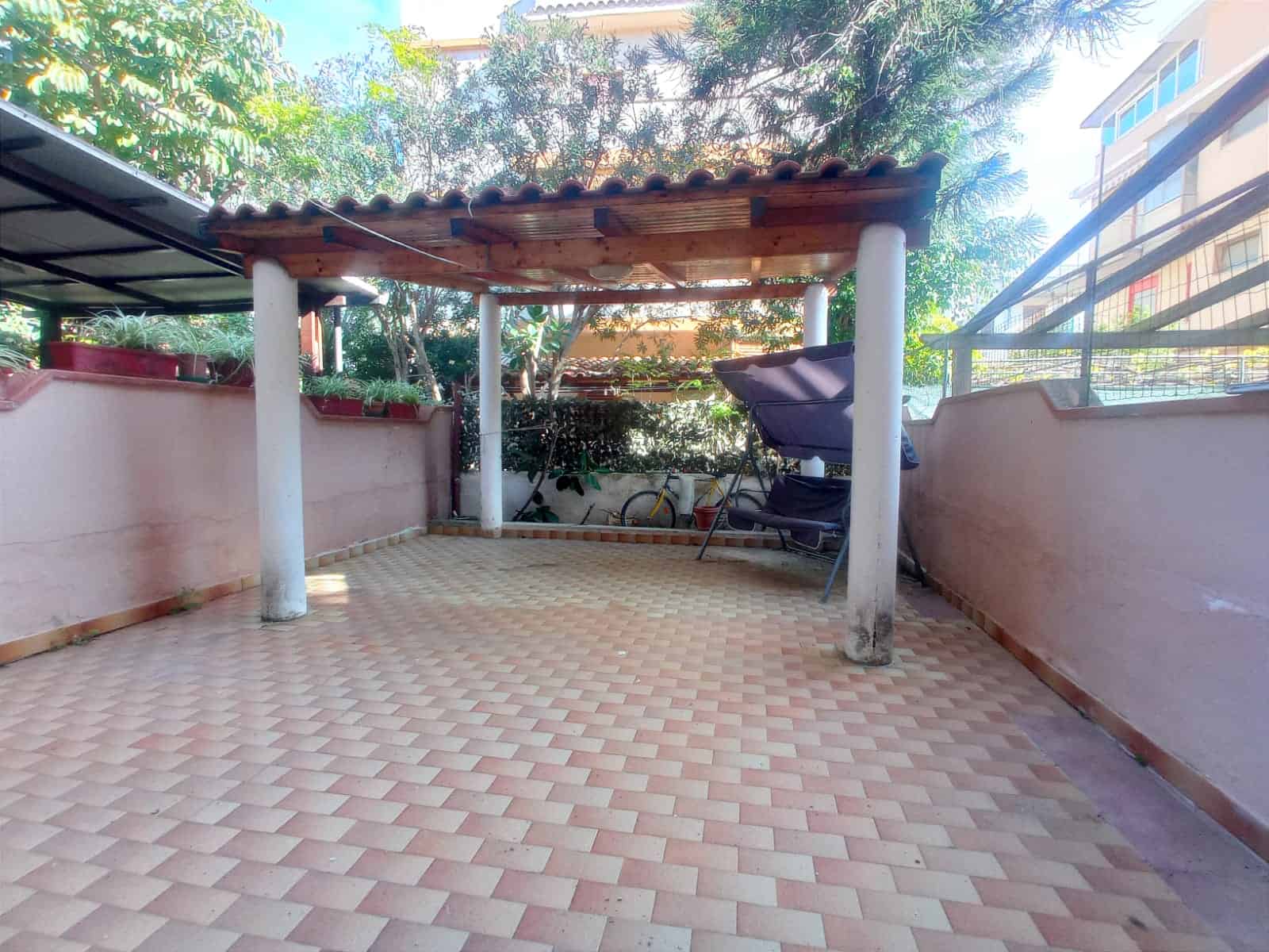 Spazio esterno con pergolato in legno, terrazza pavimentata e piante ornamentali, ideale per relax e incontri all'aperto in zona residenziale.