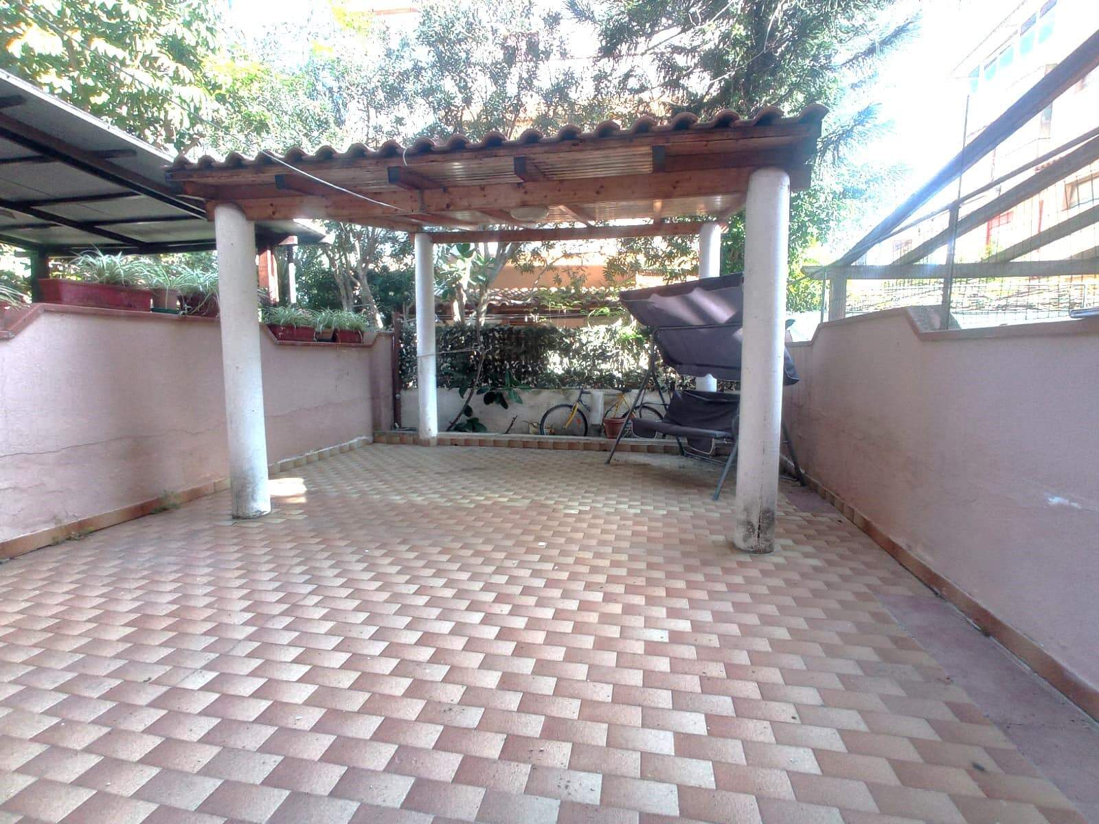 Tettoia e terrazza con pavimentazione in piastrelle beige, spazio esterno con muretti e piante, ideale per relax e momenti all'aperto.
