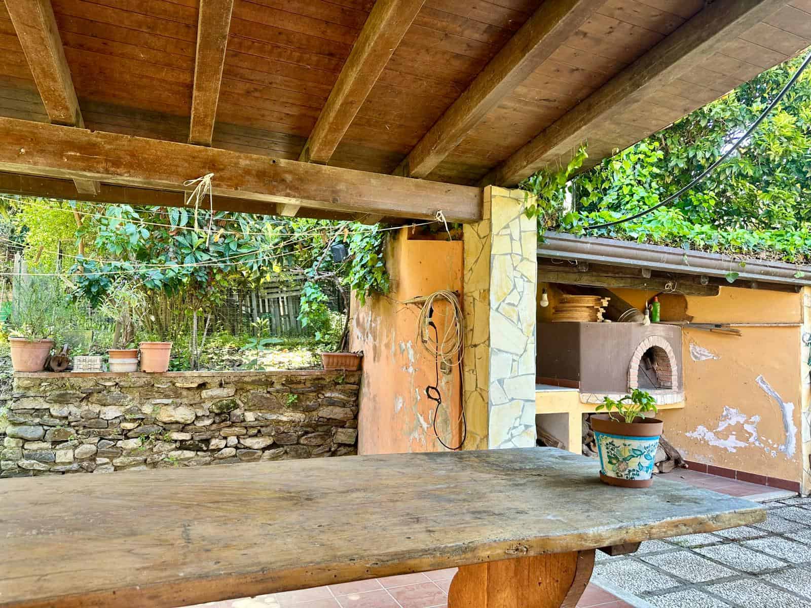 Rustico in pietra con barbecue all'aperto e zona pranzo sotto portico, immerso nel verde, ideale per eventi e barbecue all'aperto.