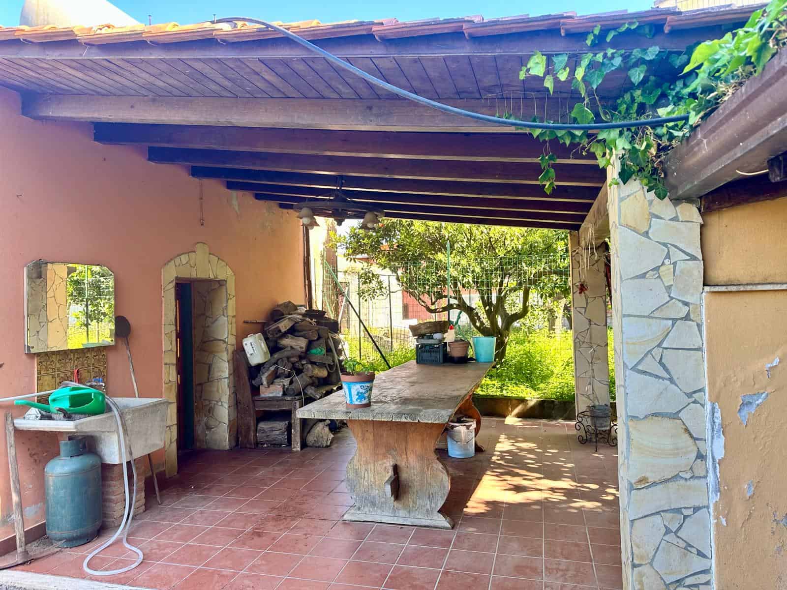 Pompeia, area esterna coperta con tavolo in legno, piante e vista giardino, stile rustico, ideale per relax e convivialità.