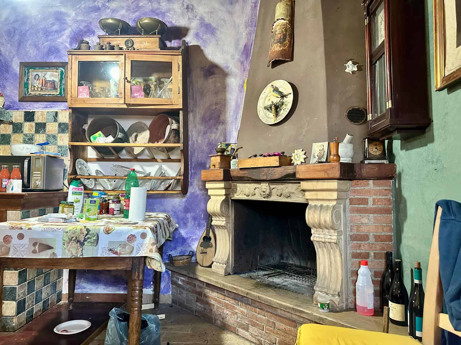 Vecchia cucina rustica con camino in pietra, pareti colorate e cucina in stile tradizionale, decorate con oggetti d'epoca e utensili da cucina, atmosfera accogliente e calorosa.