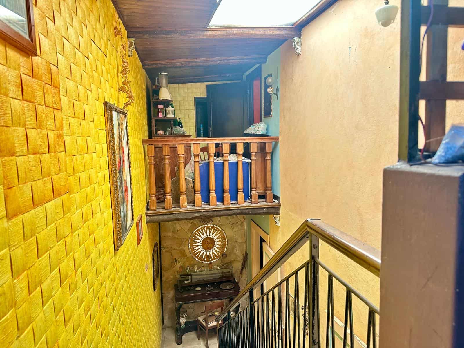 Colorato interno di una casa con parete in mattoni gialli, stile vintage, e scale in ferro battuto, atmosfera accogliente e rustica, ideale per chi cerca soluzioni di arredamento uniche e calde.