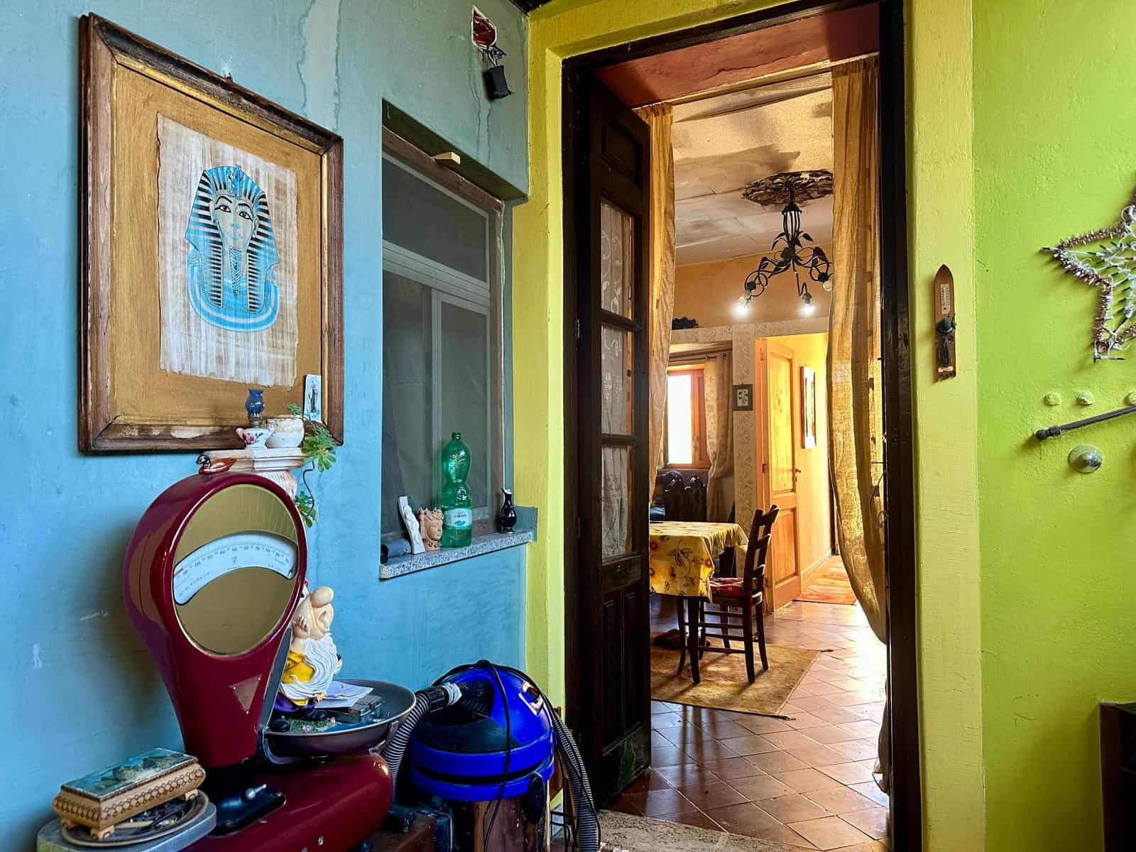 Perversa e colorata camera da pranzo con pareti verdi e azzurre, decorazioni artistiche, mobili in legno, illuminazione calda e dettagli vintage, ambientazione accogliente e vivace.