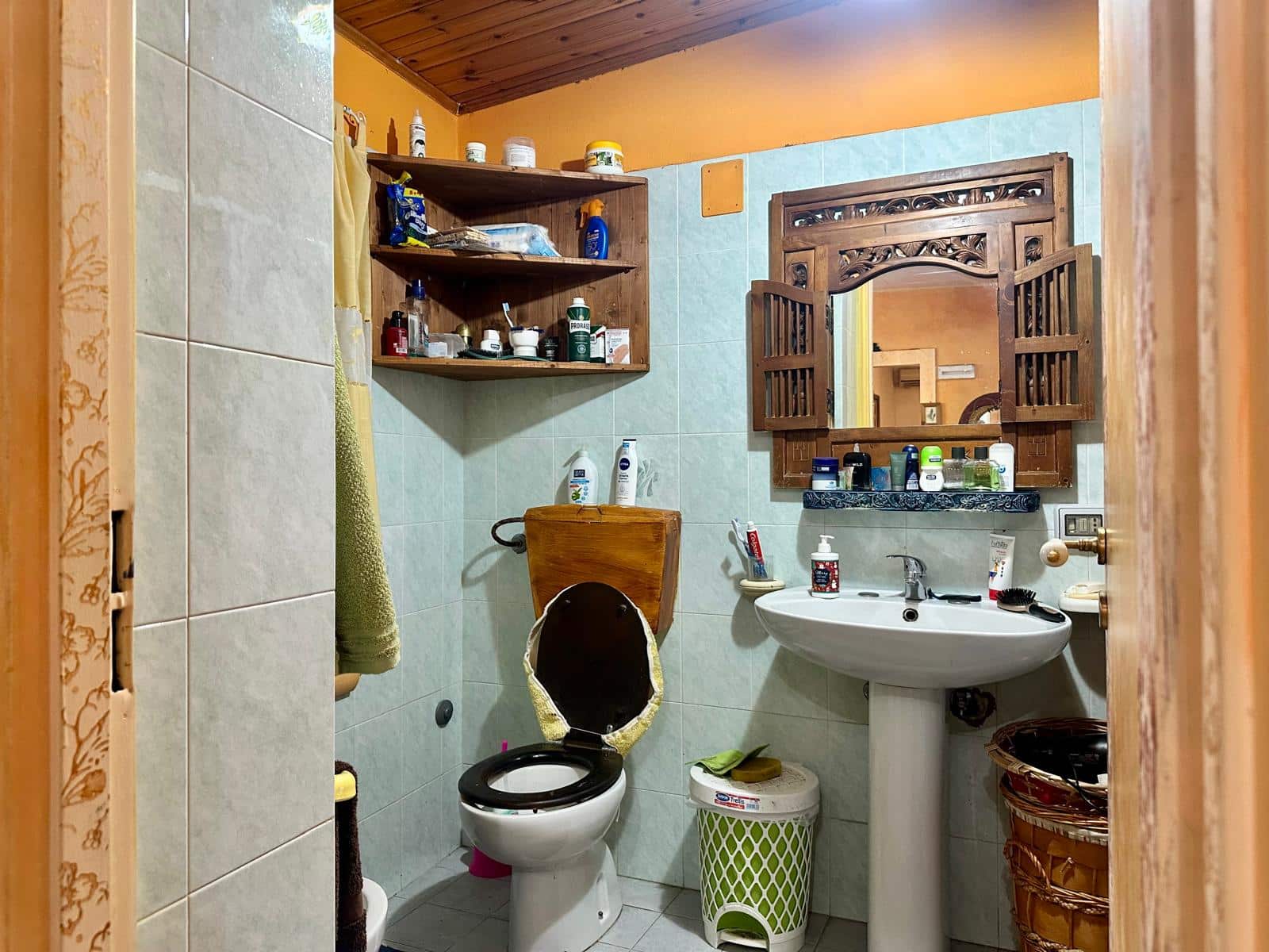 Spazio bagno rustico con arredo in legno, lavabo, specchio decorato, servizi e accessori vari, esempio di bagno tradizionale in stile country italiano.